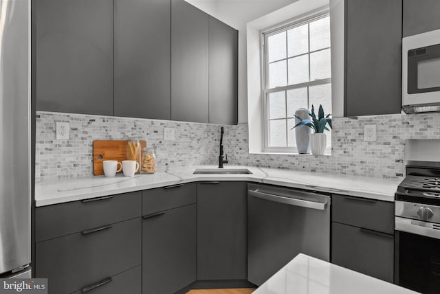 kitchen with appliances with stainless steel finishes, gray cabinets, a sink, and tasteful backsplash