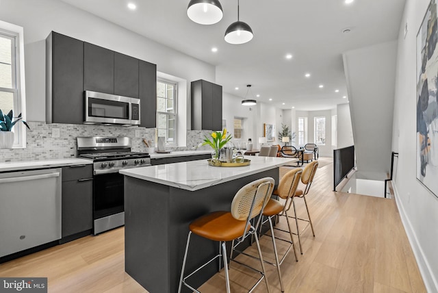 kitchen featuring tasteful backsplash, decorative light fixtures, a center island, stainless steel appliances, and light wood-style floors