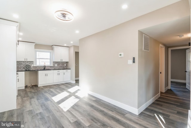 kitchen with tasteful backsplash, white cabinetry, sink, and hardwood / wood-style flooring