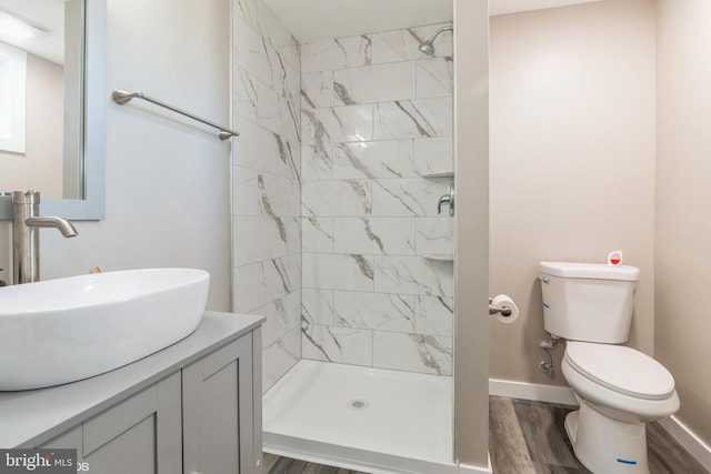 bathroom with hardwood / wood-style flooring, vanity, toilet, and a tile shower