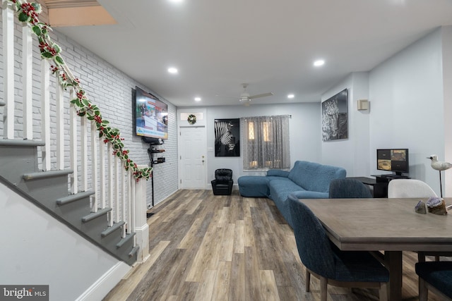 living room with ceiling fan, wood-type flooring, and brick wall