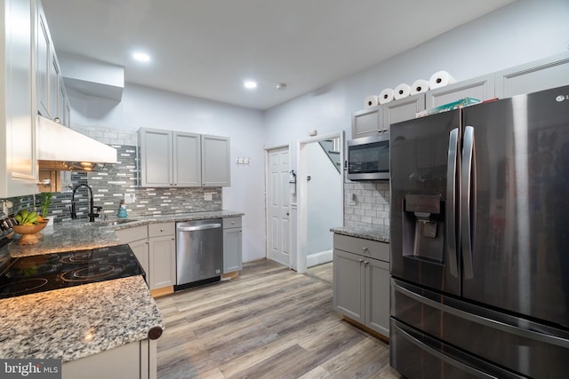 kitchen with gray cabinetry, sink, stainless steel appliances, light stone counters, and light hardwood / wood-style flooring