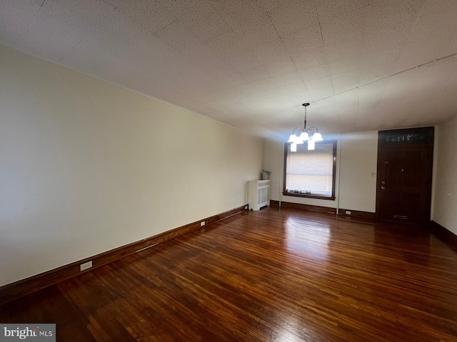 spare room with an inviting chandelier, radiator, and dark wood-type flooring