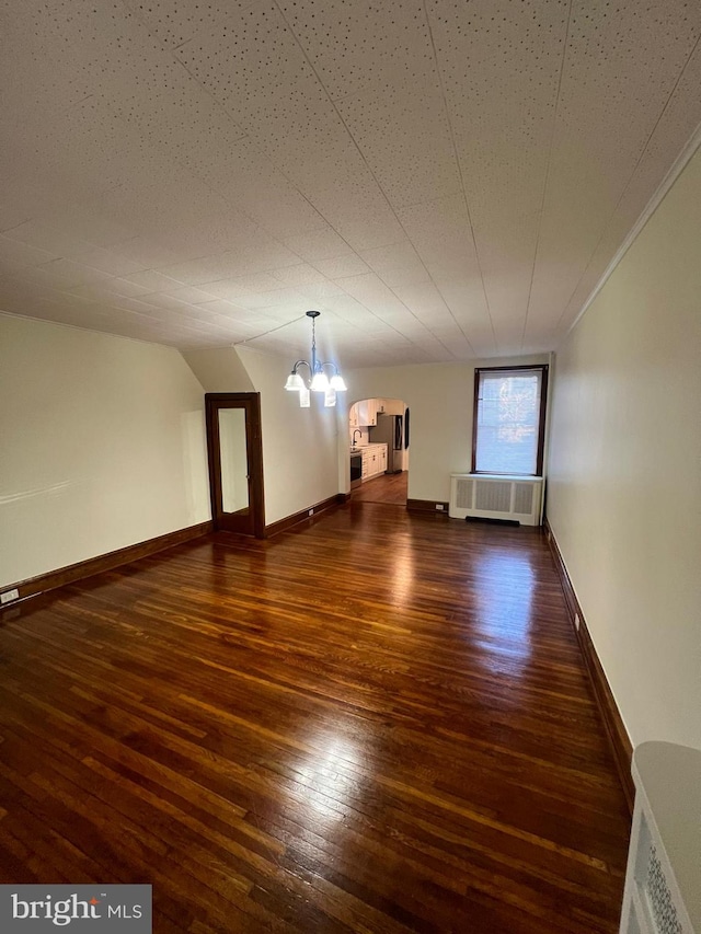 unfurnished room featuring radiator heating unit, an inviting chandelier, and dark wood-type flooring