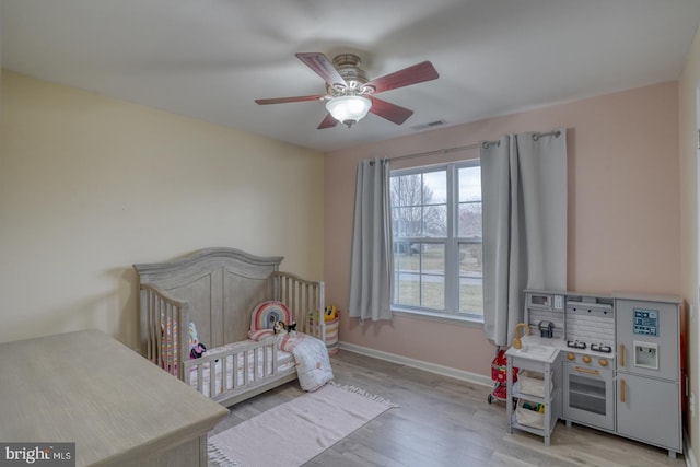 bedroom featuring ceiling fan, light hardwood / wood-style flooring, and a crib