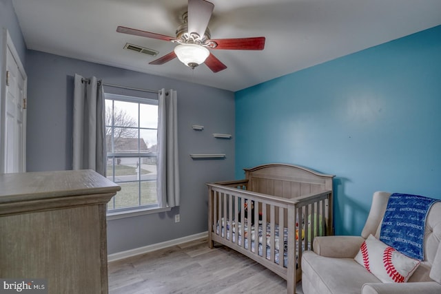 bedroom featuring multiple windows, ceiling fan, light hardwood / wood-style flooring, and a crib