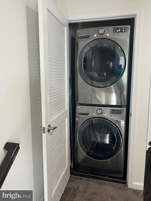 laundry room featuring dark colored carpet and stacked washer and dryer