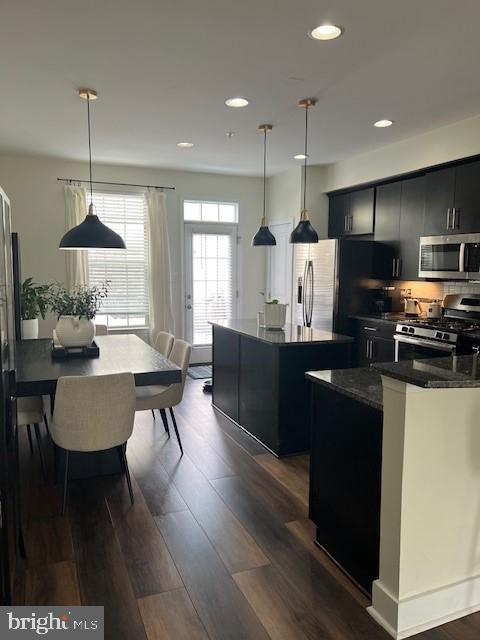 kitchen with pendant lighting, a kitchen island, appliances with stainless steel finishes, and dark wood-type flooring