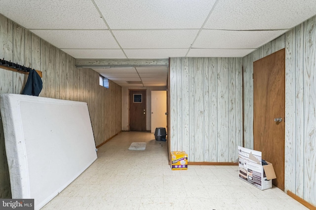 basement with a paneled ceiling and wood walls