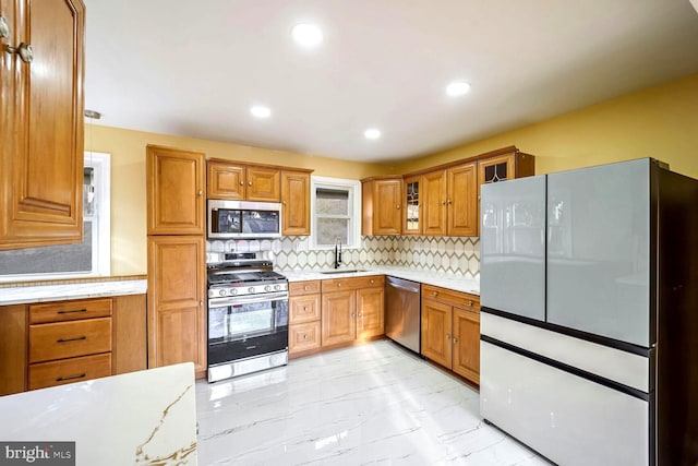 kitchen featuring light stone countertops, appliances with stainless steel finishes, backsplash, and sink