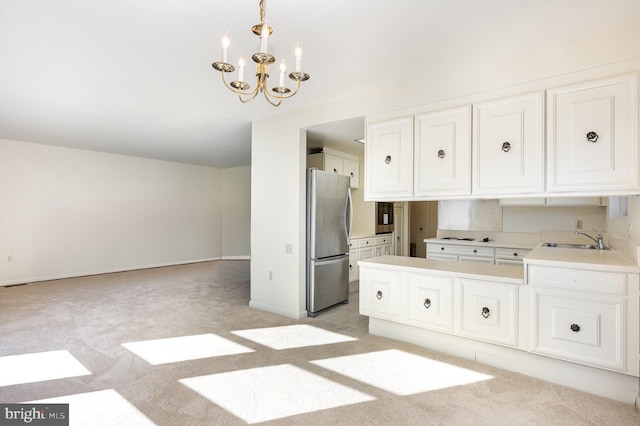 kitchen with sink, an inviting chandelier, light carpet, stainless steel refrigerator, and pendant lighting