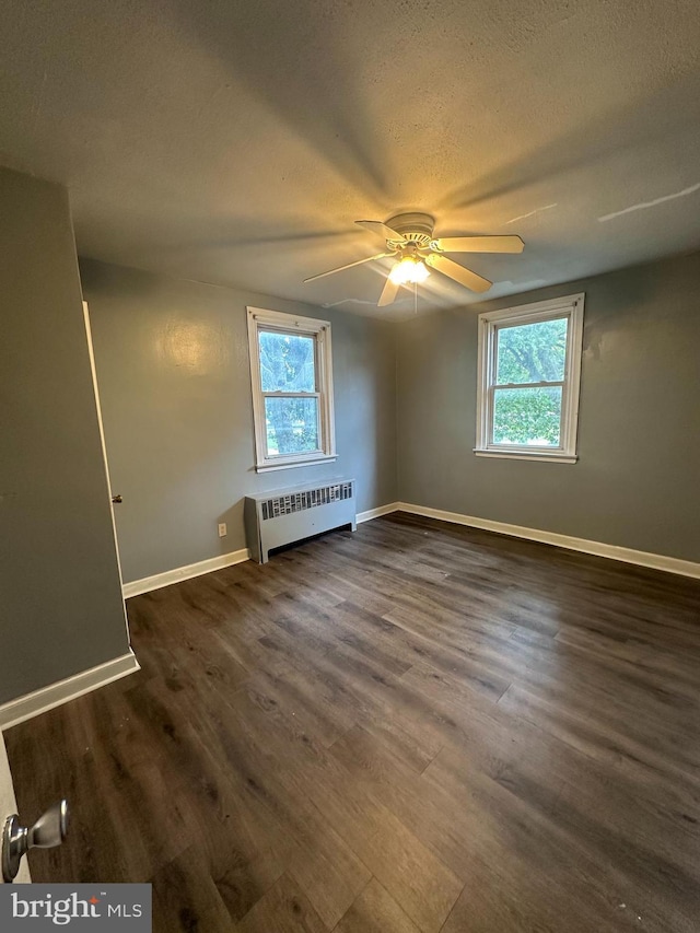 spare room with a textured ceiling, dark hardwood / wood-style floors, radiator, and ceiling fan