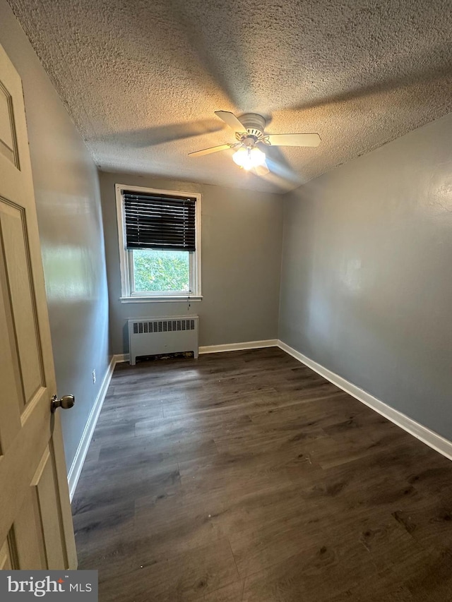 empty room with ceiling fan, dark wood-type flooring, and radiator