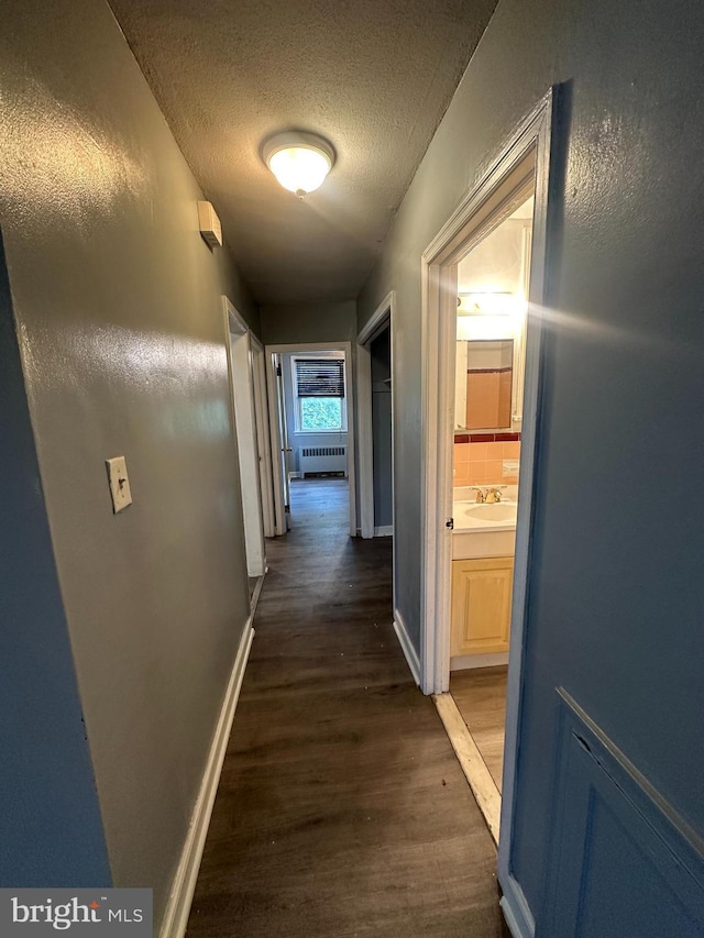 hall with a textured ceiling, sink, radiator heating unit, and dark wood-type flooring