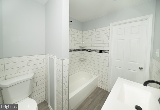 full bathroom featuring sink, tiled shower / bath, toilet, tile walls, and wood-type flooring