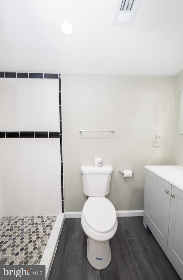 bathroom featuring hardwood / wood-style flooring, vanity, toilet, and a tile shower