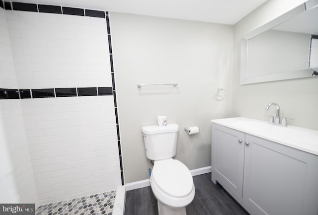 bathroom featuring hardwood / wood-style floors, vanity, toilet, and a tile shower