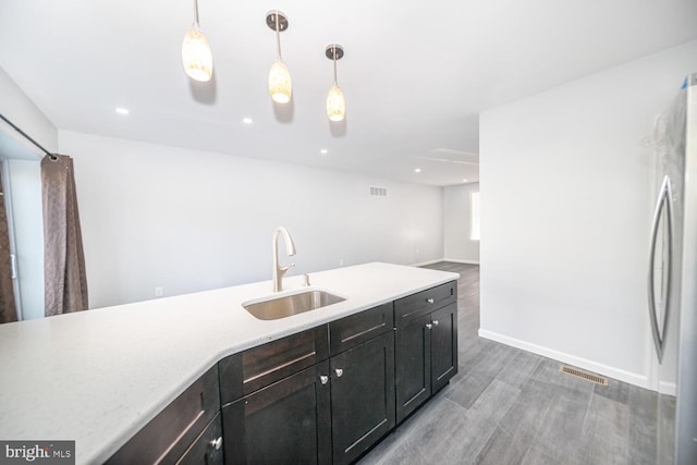 kitchen featuring wood-type flooring, decorative light fixtures, stainless steel refrigerator, and sink