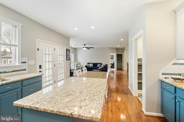 kitchen with blue cabinetry, tasteful backsplash, a center island, ceiling fan, and light hardwood / wood-style floors