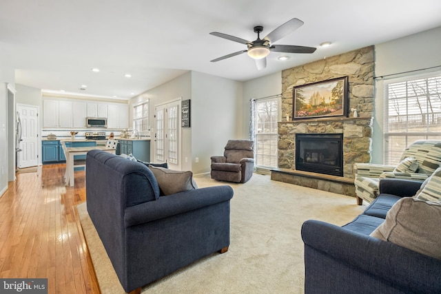 living room with sink, a stone fireplace, light hardwood / wood-style flooring, and ceiling fan