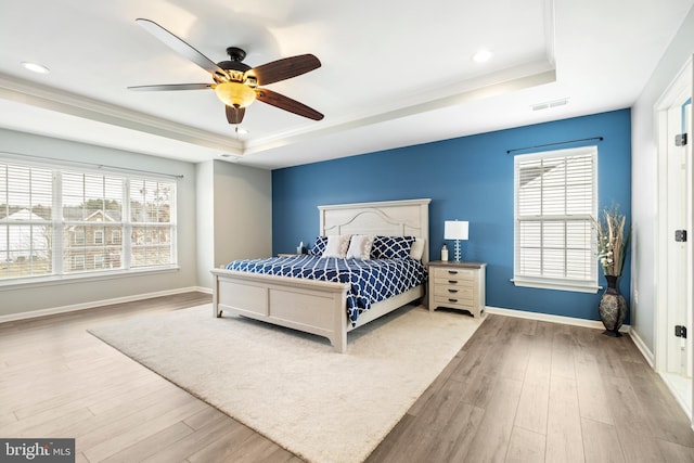 bedroom with a raised ceiling, multiple windows, and light hardwood / wood-style floors