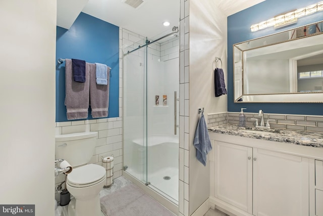 bathroom featuring vanity, toilet, a shower with shower door, and tile walls