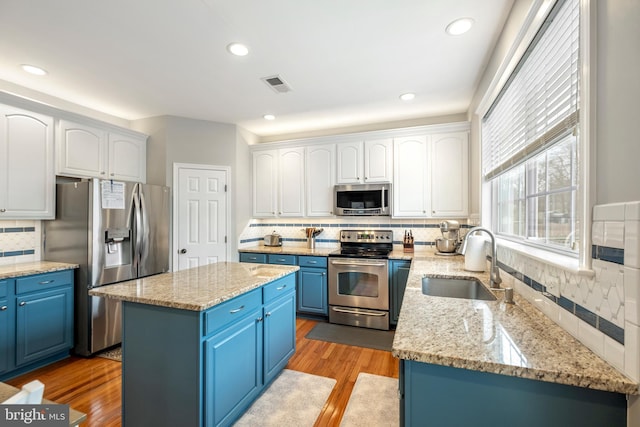 kitchen featuring blue cabinetry, sink, white cabinetry, light hardwood / wood-style flooring, and appliances with stainless steel finishes