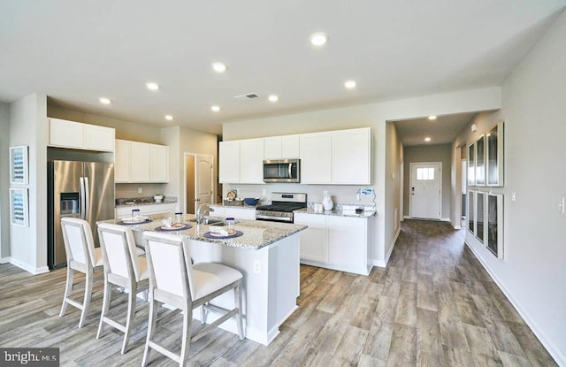 kitchen featuring white cabinets, stainless steel appliances, light stone counters, and a kitchen island with sink