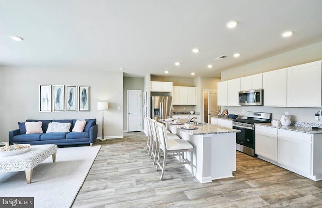 kitchen featuring white cabinetry, a kitchen island with sink, light stone countertops, and stainless steel appliances