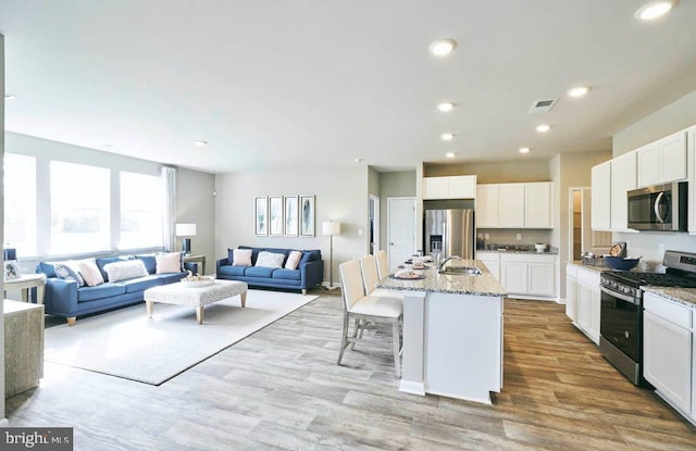 kitchen with a kitchen bar, appliances with stainless steel finishes, light stone countertops, a center island with sink, and white cabinets