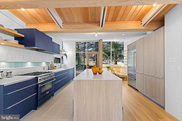 kitchen with high end appliances, a kitchen island, extractor fan, blue cabinetry, and open shelves