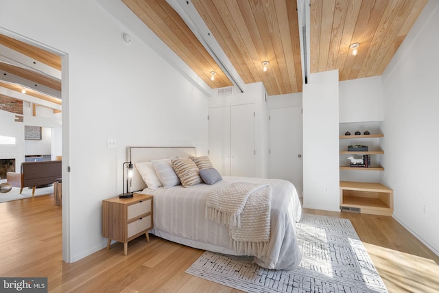 bedroom featuring wood finished floors, visible vents, wood ceiling, a brick fireplace, and beam ceiling