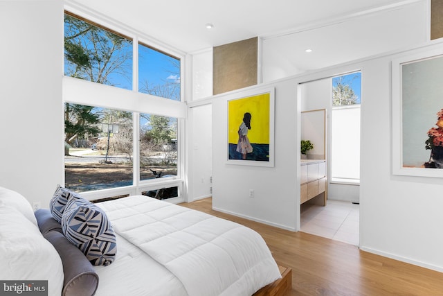 bedroom featuring a wall of windows, connected bathroom, baseboards, and wood finished floors