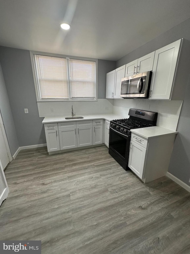 kitchen with black range with gas stovetop, white cabinetry, sink, and light wood-type flooring