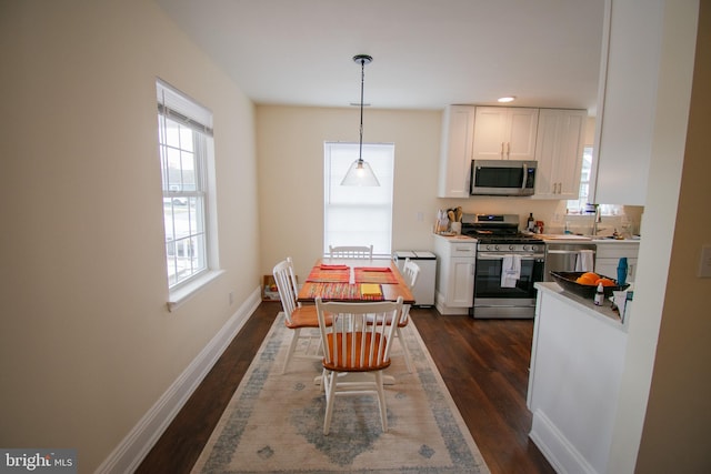 kitchen featuring white cabinets, dark wood-style floors, decorative light fixtures, stainless steel appliances, and light countertops