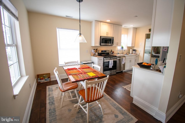 kitchen featuring white cabinets, appliances with stainless steel finishes, dark wood-type flooring, and pendant lighting