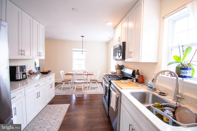 kitchen with decorative light fixtures, sink, white cabinetry, and stainless steel appliances