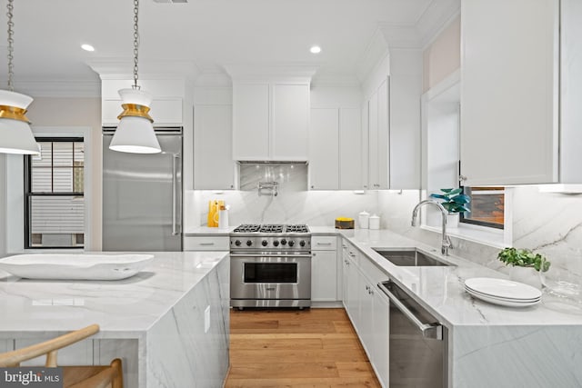 kitchen with light stone countertops, sink, decorative light fixtures, white cabinets, and high end appliances