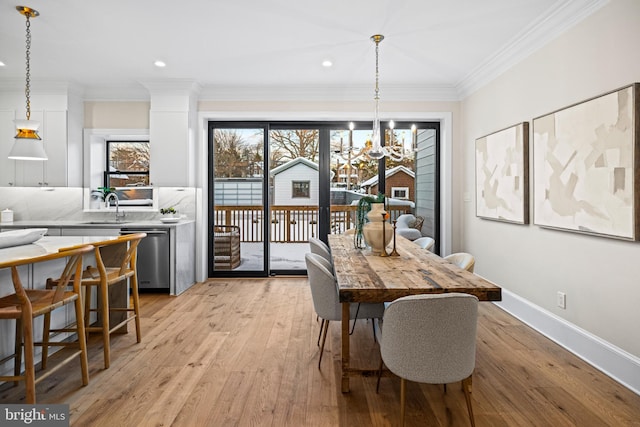 dining area featuring sink, an inviting chandelier, light hardwood / wood-style flooring, and ornamental molding