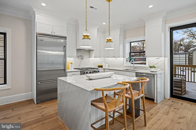 kitchen with hanging light fixtures, stainless steel appliances, a kitchen island, white cabinets, and light wood-type flooring