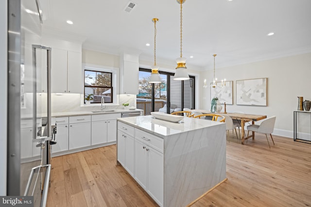 kitchen featuring sink, a kitchen island, light hardwood / wood-style floors, decorative light fixtures, and white cabinets