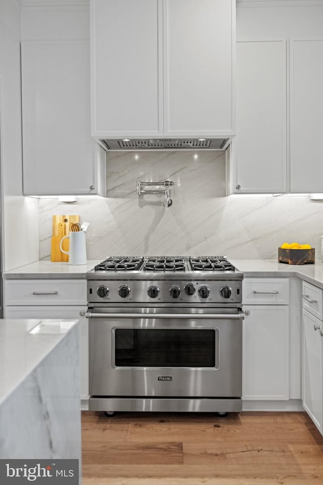 kitchen featuring exhaust hood, high end stainless steel range oven, decorative backsplash, light stone counters, and white cabinetry