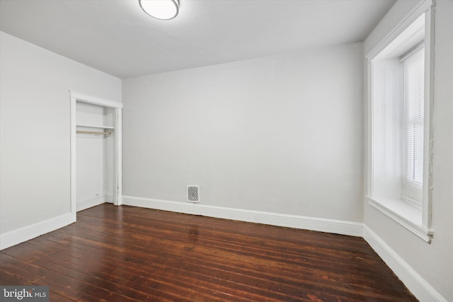 unfurnished bedroom featuring dark hardwood / wood-style floors, multiple windows, and a closet