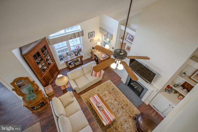 living room with built in shelves, a towering ceiling, and dark wood-type flooring