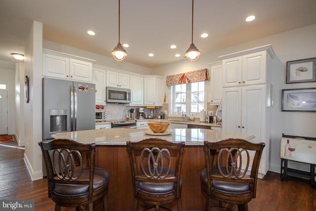 kitchen with a center island, white cabinets, pendant lighting, and appliances with stainless steel finishes