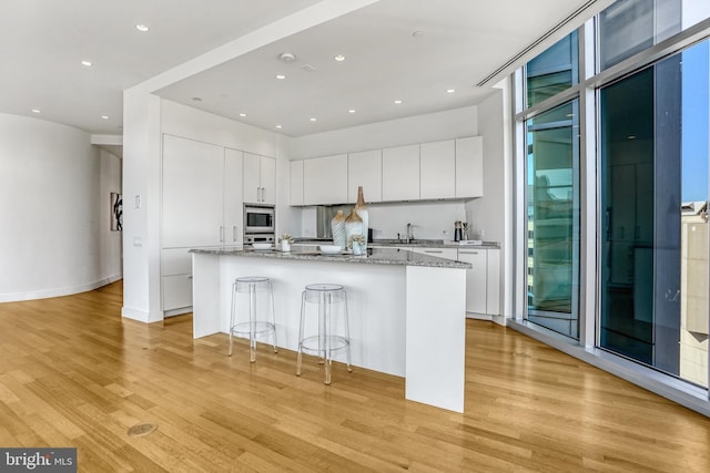 kitchen featuring light stone countertops, white cabinetry, appliances with stainless steel finishes, and a center island with sink