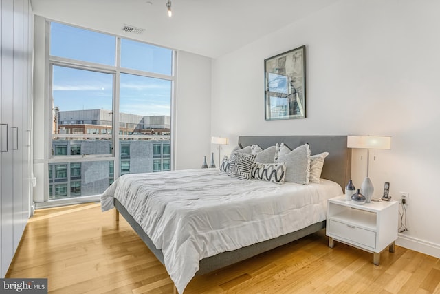 bedroom with a wall of windows and light hardwood / wood-style flooring