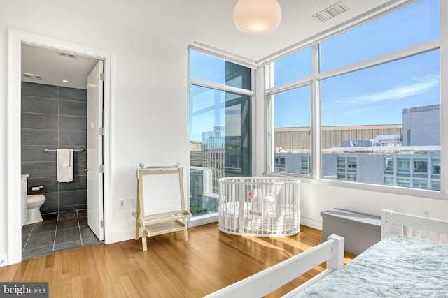 bedroom featuring connected bathroom, hardwood / wood-style floors, and tile walls