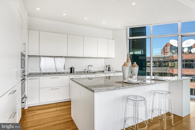 kitchen featuring white cabinetry, light hardwood / wood-style flooring, light stone countertops, and appliances with stainless steel finishes