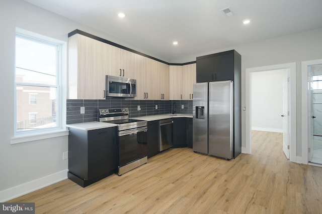 kitchen featuring sink, light brown cabinets, light hardwood / wood-style flooring, backsplash, and appliances with stainless steel finishes